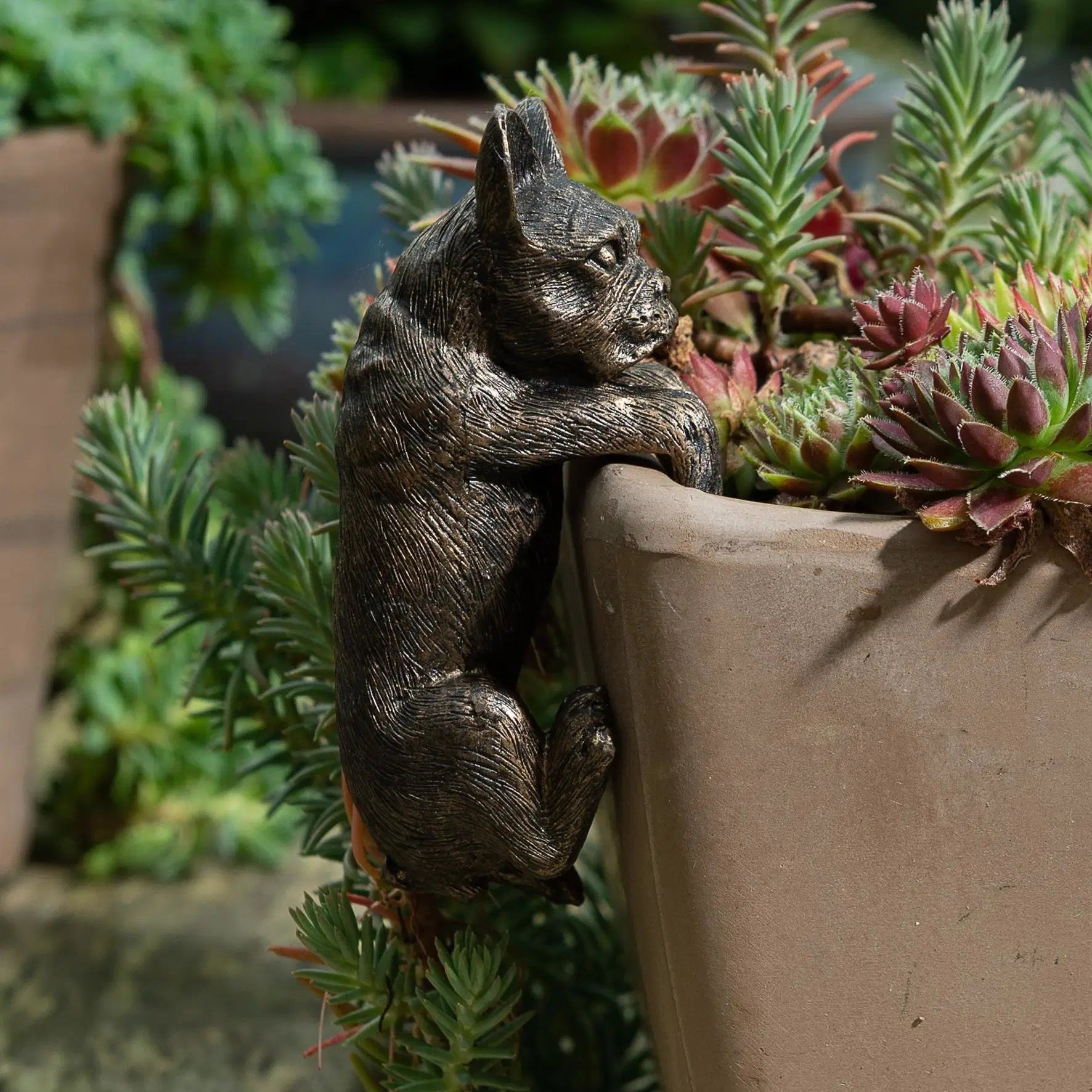 Bronze french bulldog figurine on a plant pot with greenery in the background